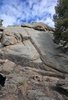 Large rocky outcrop with a small fire burning at its base and a black and white dog in the lower left foreground under a partly cloudy blue sky