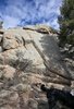 Large sunlit rock formation surrounded by trees with a black and white border collie partially visible in the foreground under a bright blue sky with scattered clouds