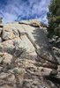 Large rock formation with shadows of trees cast on its surface under a partly cloudy blue sky