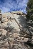 Large light gray rock formation surrounded by pine trees under a partly cloudy blue sky