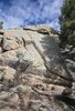 Large sunlit rock formation with shadows of tree branches and a partly cloudy blue sky above