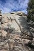 Large sunlit granite rock formation with shadows of nearby pine trees cast on its surface under a partly cloudy blue sky