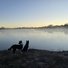 Two border collies standing on frosty grass looking out over a misty river at sunrise