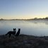 Two border collies standing on frosty ground by a calm river with mist rising, under a clear early morning sky at sunrise