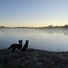Two border collies standing and sitting on a frosty shore looking out over a calm, mist-covered river at dawn