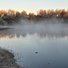 Calm river reflecting leafless trees with a layer of mist rising from the water in the early morning light