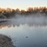 Calm river with early morning mist rising, bare trees with golden light on their branches reflecting on the water
