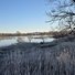 Calm river bordered by frosted grasses and leafless trees under a clear blue sky