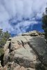 close-up of large weathered rock formations surrounded by pine trees under a partly cloudy blue sky