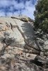 Large granite rock formation with a small campfire burning at its base, surrounded by dry grass and pine trees under a partly cloudy sky