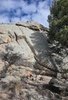 Large rocky outcrop with patches of moss and surrounding evergreen trees under a partly cloudy sky