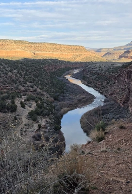 A winding river flowing through a deep canyon with layered rocky cliffs and sparse vegetation under a partly cloudy sky