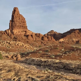 massive red rock formation rising prominently with layered cliffs and sparse desert vegetation under a partly cloudy sky