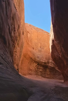 Narrow canyon passage with smooth, reddish sandstone walls curving inward under a clear blue sky