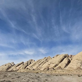 Uplifted sedimentary rock formations under a blue sky with wispy clouds above a desert landscape