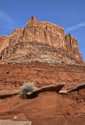 massive red sandstone cliff with layers of sedimentary rock under a clear blue sky