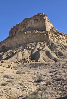 Sedimentary rock formation rising steeply under a clear blue sky with sparse desert vegetation in the foreground
