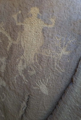 Petroglyph carvings on rock showing a human figure with raised arms, an animal with antlers, and a handprint