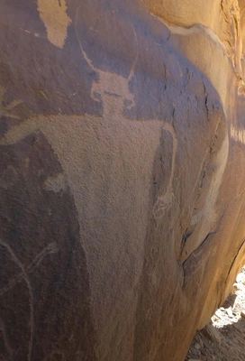 ancient petroglyph carved into a rock surface depicting a figure with raised arms and two horn-like shapes on its head