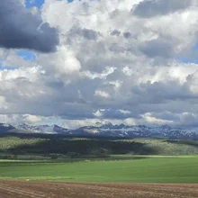 Cloudy sky over green fields and snow-capped mountain range in the distance