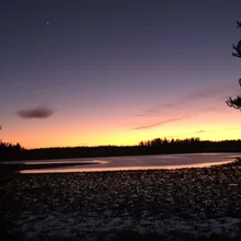calm lake at dusk with a gradient sky from yellow near the horizon to deep purple above, framed by silhouetted trees