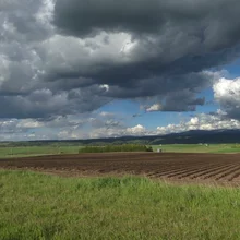 expansive farmland under a dramatic sky filled with large, dark clouds and patches of blue