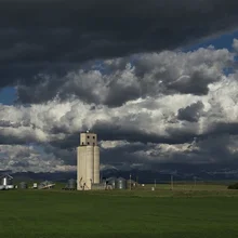 Tall industrial silo under a dramatic cloudy sky with green grass in the foreground
