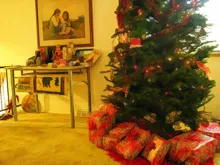 Christmas tree with red and white wrapped gifts underneath in a carpeted room with a table and framed artwork on the wall