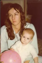 woman with long brown hair holding a baby who is holding a pink ball with orange spots