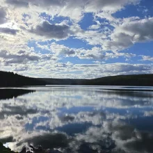 Calm lake reflecting a sky filled with scattered clouds and surrounded by forested hills