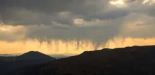Dark clouds with rain falling over mountain silhouettes at sunset