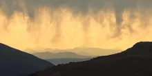 Mountain silhouettes under a sky with dramatic clouds illuminated by soft golden light