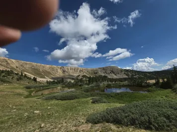 mountain landscape with two small reflective ponds surrounded by green vegetation under a blue sky with scattered white clouds