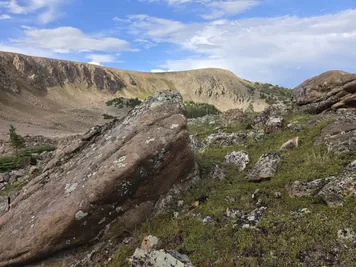 Rocky mountain terrain with large boulders and sparse greenery under a partly cloudy sky